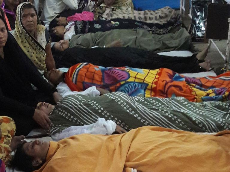 Frauen liegen nach der Operation schlafend auf dem Gang. An ihren Köpfen wachen Verwandte.