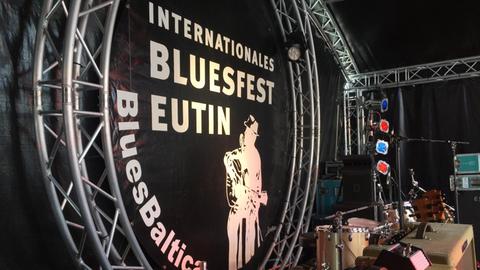 Das Banner des Bluesfestivals Eutin hängt groß über der Bühne, davor stehen Gitarrenverstärker.