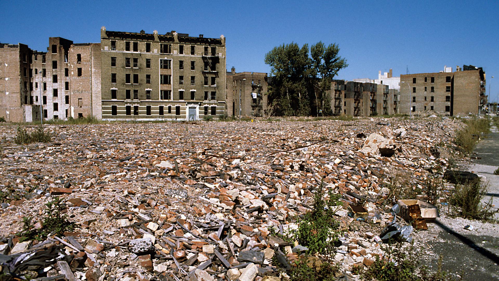 Blick über eine weitläufige Fläche mit Bauschutt und Müll auf verfallene, ehemals mehrstöckige Wohnhäuser im New Yorker Stadtteil Bronx. (Undatierte Aufnahme).