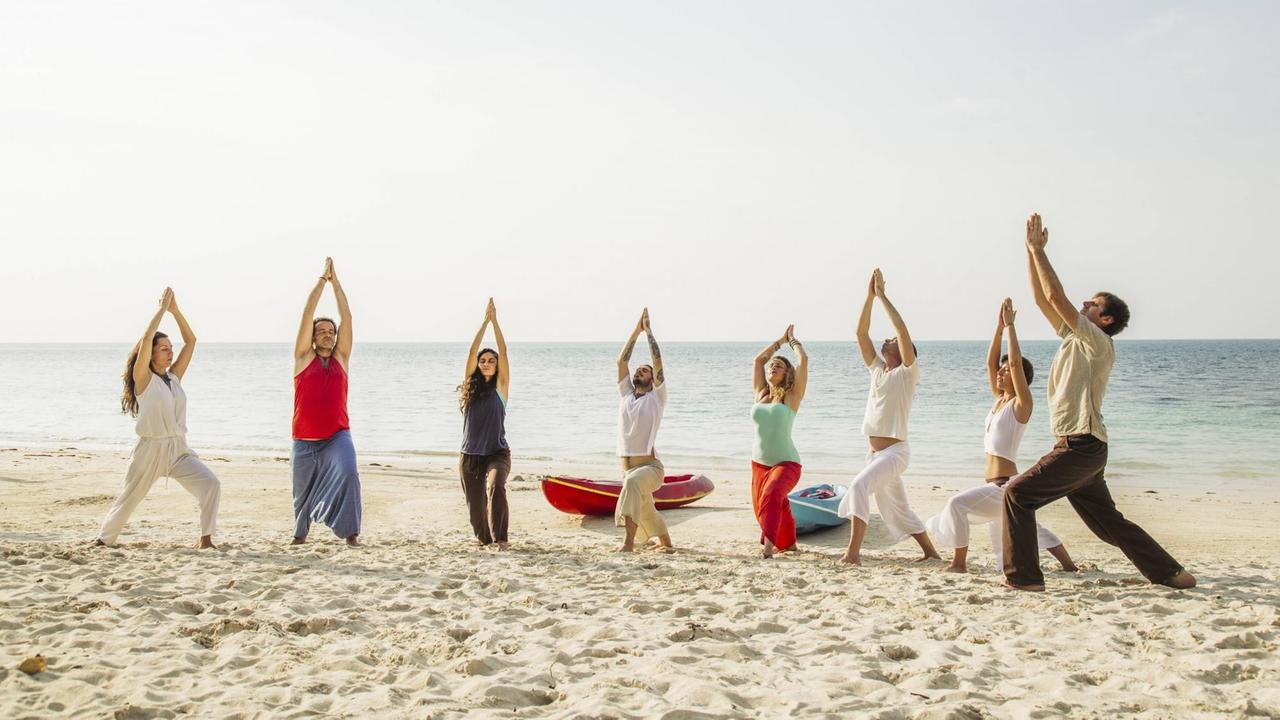 Eine Gruppe Menschen macht Yoga am Strand.