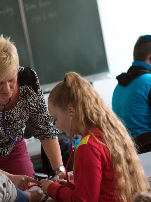 Die Lehrerin für Altenpflege am Institut für Weiterbildung in der Kranken- und Altenpflege zeigt in Magdeburg in einem Klassenraum zwei Schülerinnen den Umgang mit einem Blutdruckmessgerät