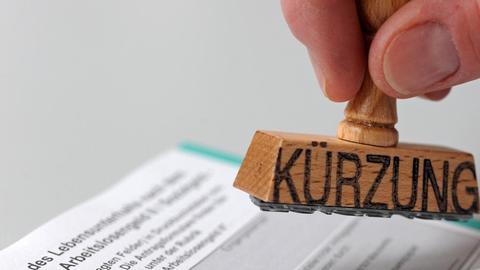 ILLUSTRATION - Ein Mann hält am Mittwoch (16.06.2010) einen Stempel, auf dem das Wort "Kürzung" steht, über ein Formular zur Beantragung von Arbeitslosengeld II (ALG II), umgangssprachlich auch "Hartz IV" genannt. Das Alg II ist die Grundsicherung für erwerbsfähige Hilfebedürftige nach dem Sozialgesetzbuch II (SGB II). Foto: Andreas Gebert dpa/lby | Verwendung weltweit