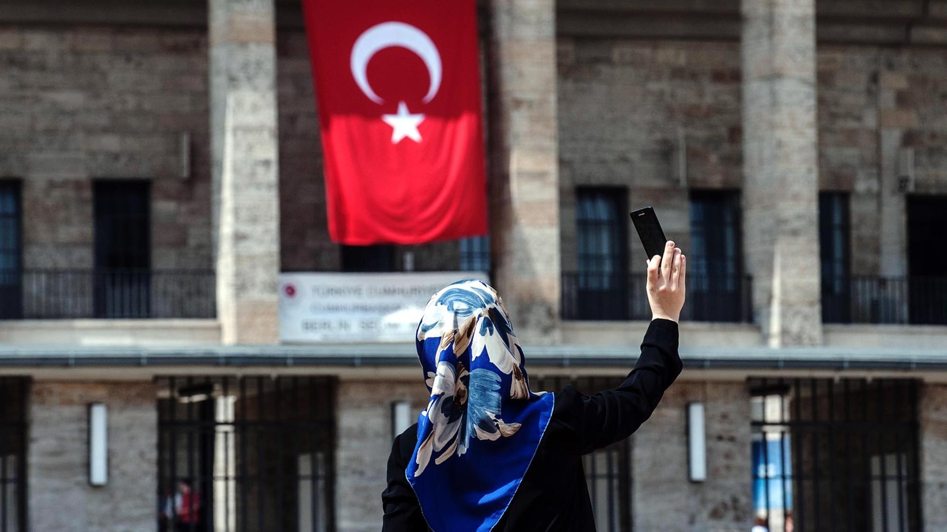 Eine Frau mit Kopftuch fotografiert sich selbst am 03.08.2014 vor dem Olympiastadion in Berlin, an dem eine türkische Fahne hängt. Im Olympiastadion ist ein Wahlzentrum für die türkische Präsidentenwahl in Deutschland. Erstmals können türkische Staatsange