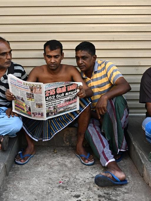 In der Nähe des St. Anthony's Shrine in Colombo sitzen vier Anwohner auf dem Boden und lesen Zeitungen, in denen über die Anschläge in Sri Lanka vom 21. April berichtet wird.