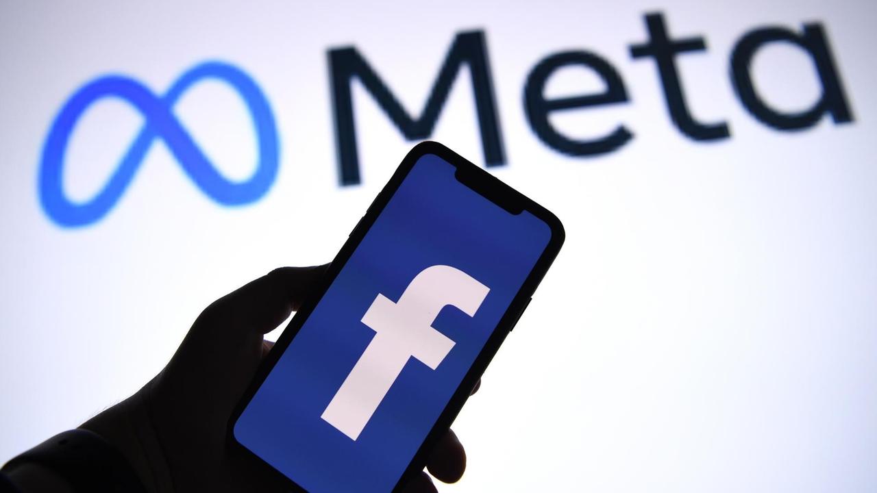 Ein Handy mit dem Facebook-Symbol auf dem Display vor einer Projektion mit dem Schriftzug "Meta"