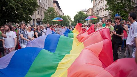 Etliche Menschen halten bei einer Protestkundgebung der Pride-Bewegung eine überdimensionale Regenbogenfahne.