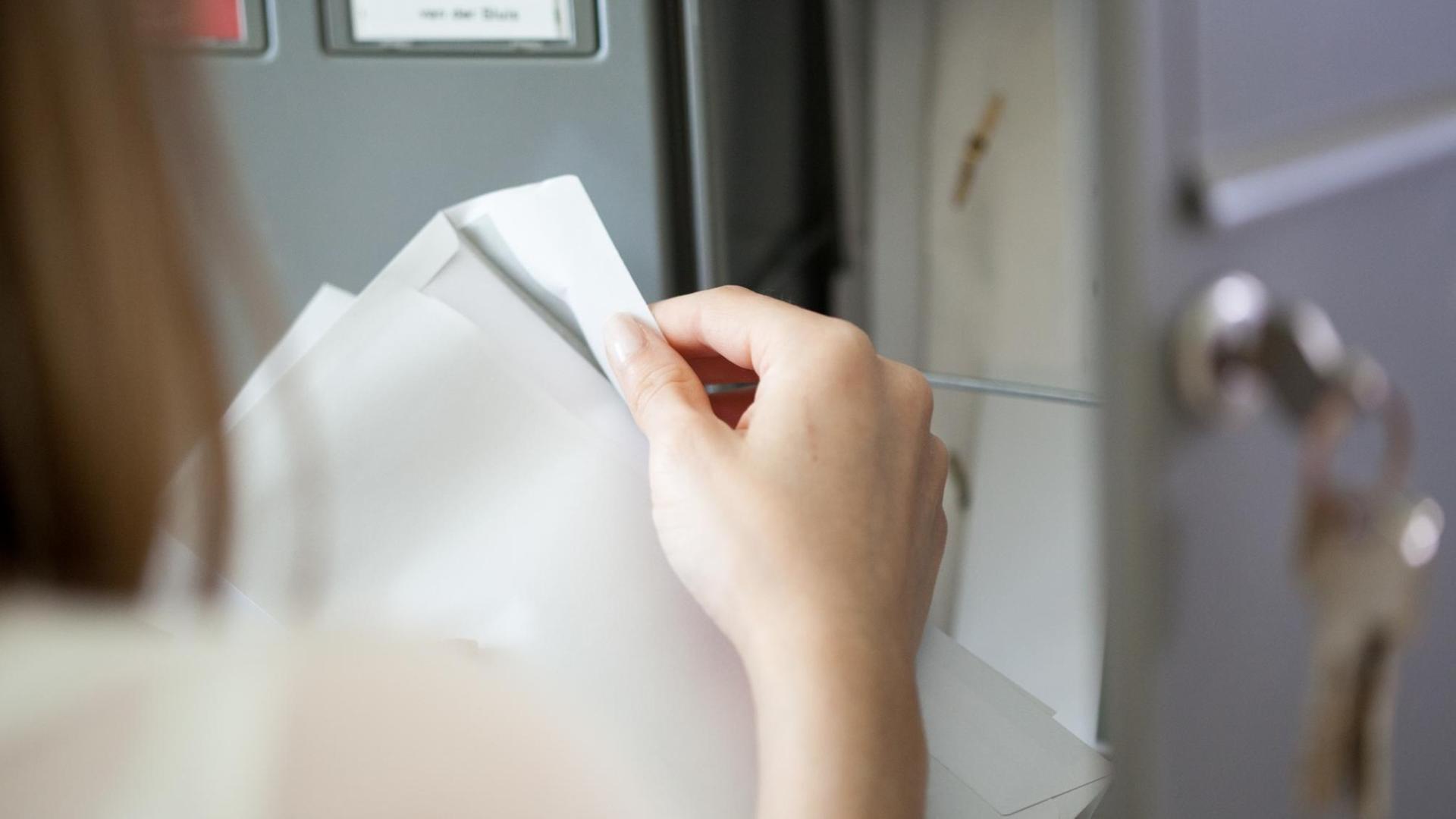Eine junge Frau öffnet einen Brief aus ihrem Briefkasten. Eine junge Frau öffnet einen Brief aus ihrem Briefkasten.