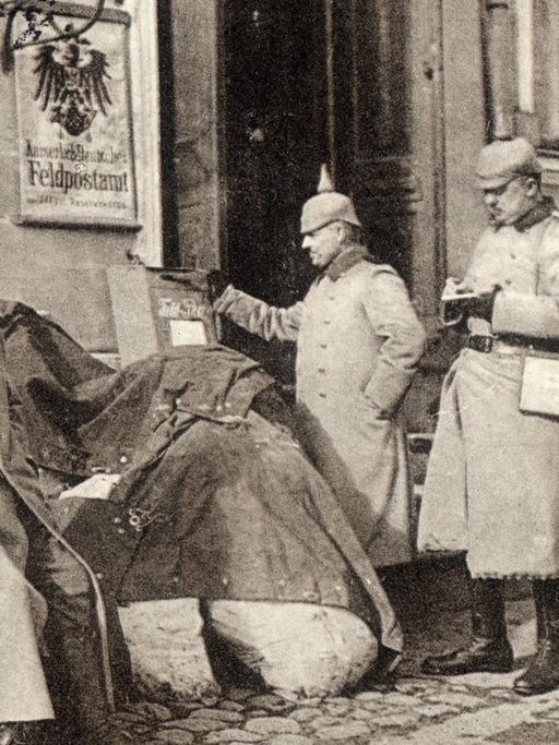 Deutsche Soldaten schreiben um 1914 vor einem Feldpostamt in Kolno Feldpostkarten. Die Karte wurde als Ostpreußenhilfe mit dem Titel "Feldpost-Sammelstelle in Kolno" verlegt und im August 1918 beschriftet.
