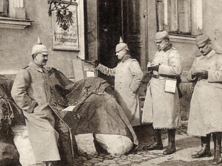 Deutsche Soldaten schreiben um 1914 vor einem Feldpostamt in Kolno Feldpostkarten. Die Karte wurde als Ostpreußenhilfe mit dem Titel "Feldpost-Sammelstelle in Kolno" verlegt und im August 1918 beschriftet.