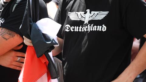 Ein Teilnehmer einer Demonstration von Rechtsextremen hält eine schwarz-weiß-rote Fahne in der Hand und trägt ein schwarzes T-Shirt mit der Aufschrift "Deutschland".