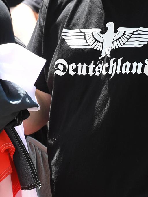 Ein Teilnehmer einer Demonstration von Rechtsextremen hält eine schwarz-weiß-rote Fahne in der Hand und trägt ein schwarzes T-Shirt mit der Aufschrift "Deutschland".