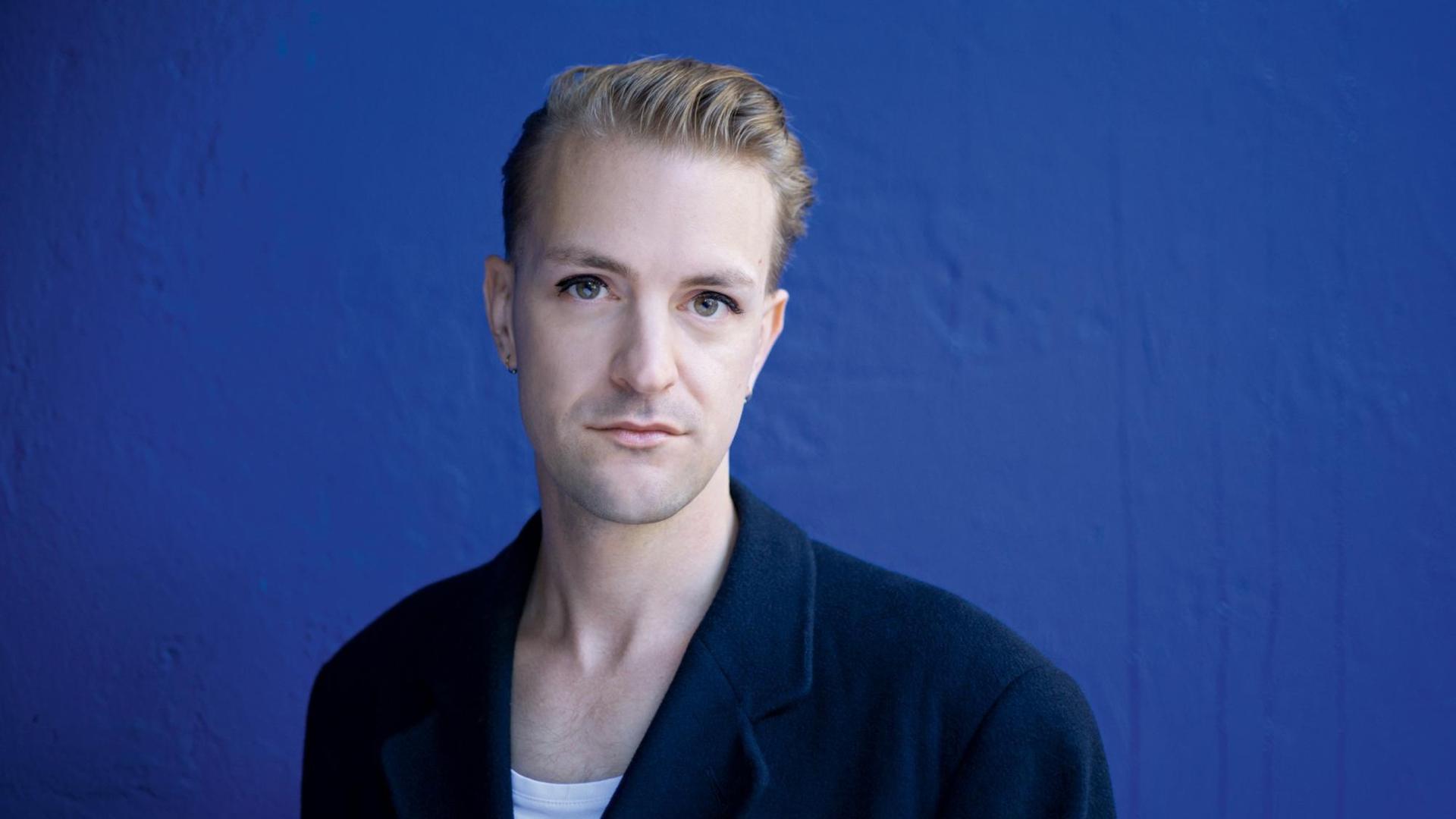 Porträt des österreichischen Musikers, Autors und Produzenten Sebastian Janata vor einer blauen Wand.