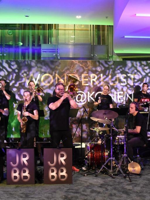 Jazzrausch Big Band auf der Bühne bei einer Veranstaltung in München. Die Band spielt, im Hintergrund grünes und violette Lichteffekte.