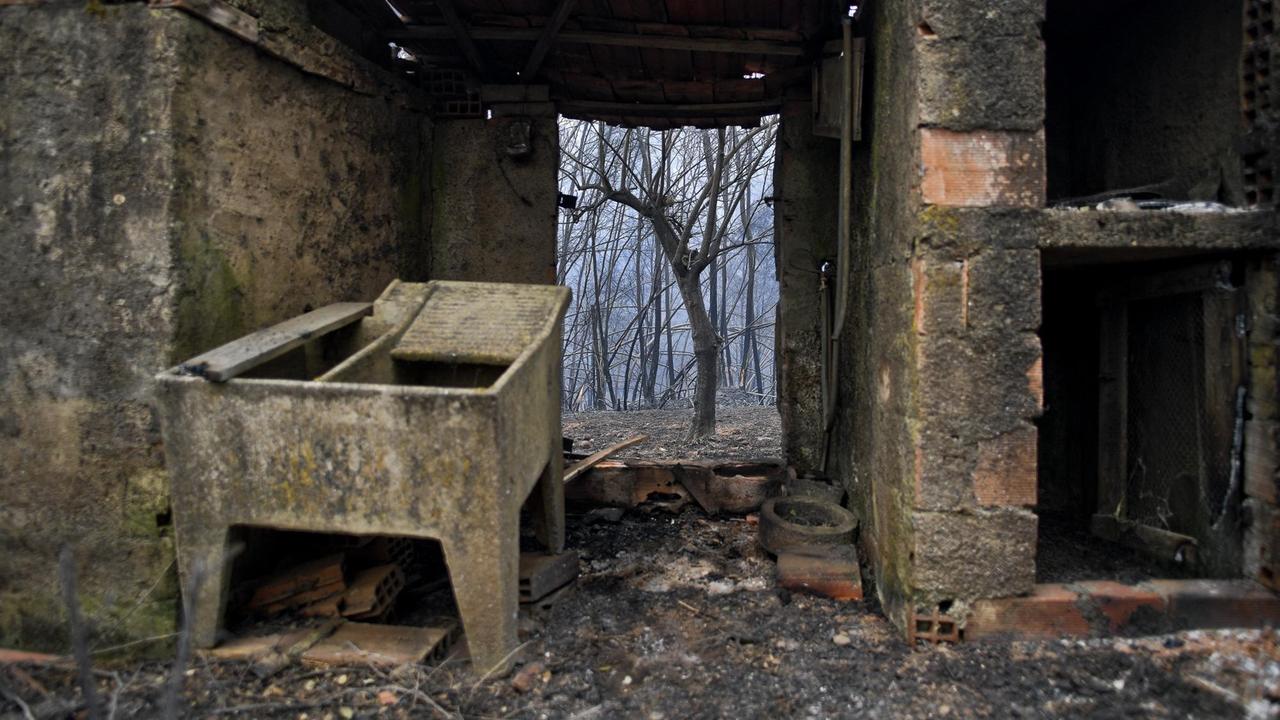 Durch die Ruinen eines abgebranntes Haus sind verkohlte Baumstämme zu sehen.
