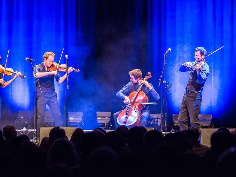 Die vier Musiker stehen auf einer grell blau erleuchteten Bühne und rocken des Publikum