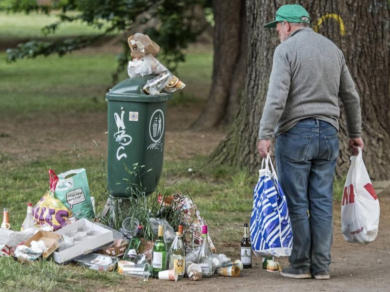 Farbfoto, ein alter Mann sammelt Flaschen vor einem städtischen Müllbehälter
