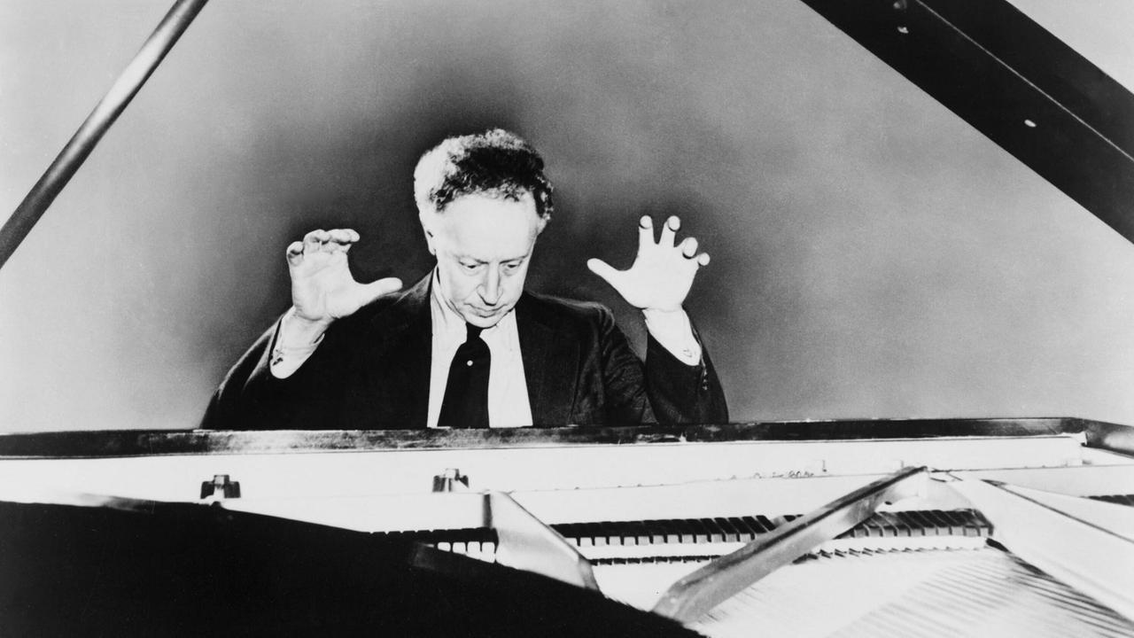 Pianist Arthur Rubinstein sitzt am Flügel im Jahr 1951 und reißt die Hände nach oben.