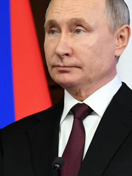 Putin in schwarzem Sacko vor der russischen Flagge