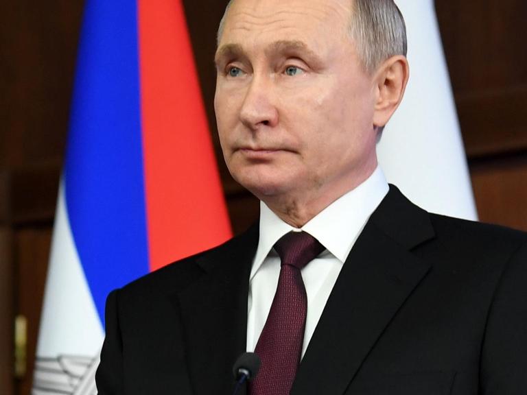 Putin in schwarzem Sacko vor der russischen Flagge