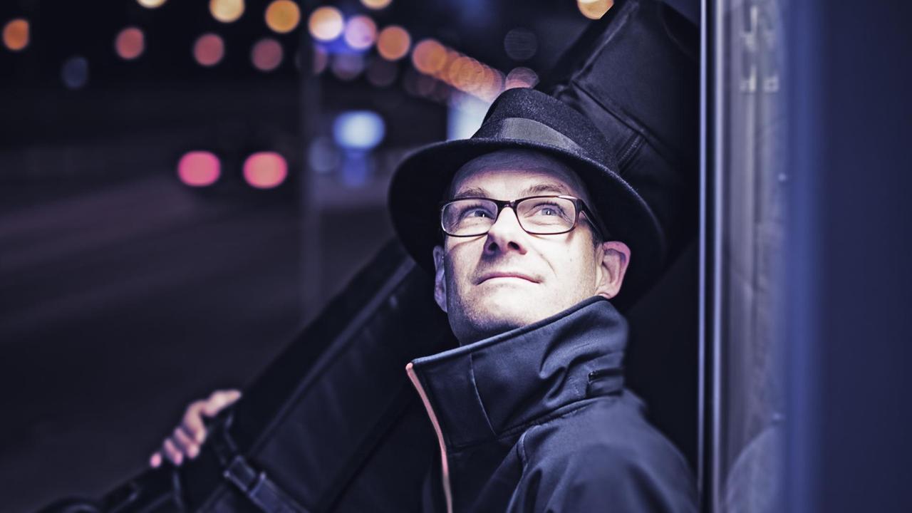 Sven Faller nachts mit seinem Kontrabass, Straßenlichter im Hintergrund