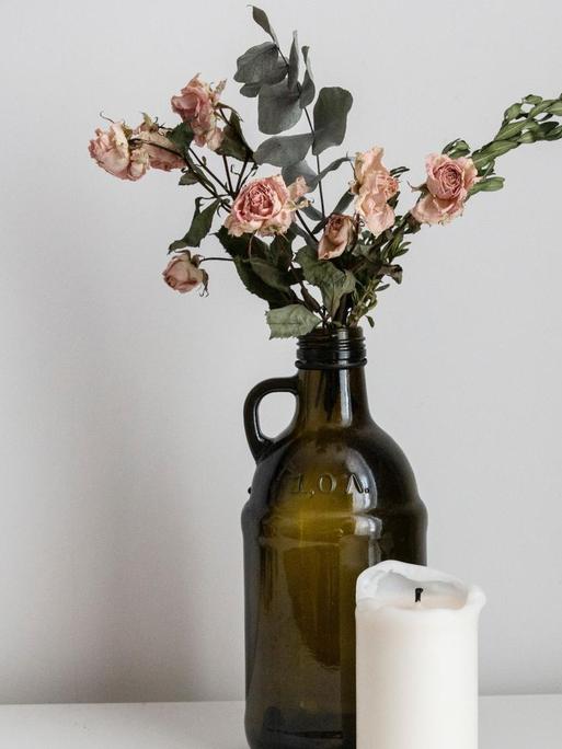 Eine Vase mit einer vertrockneten Rose und eine Kerze stehen auf einem Tisch.