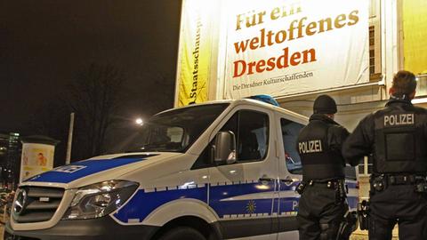 Drei Polizisten stehen in Dresden neben ihrem Einsatzwagen. 