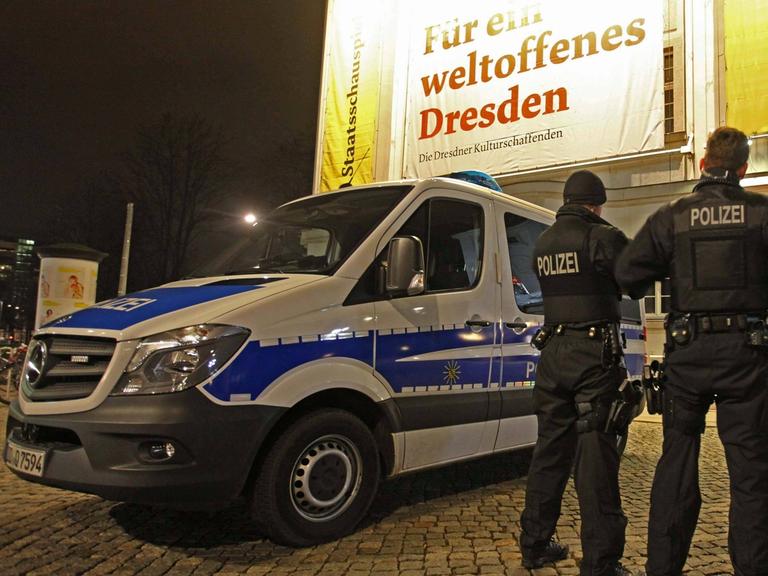 Drei Polizisten stehen in Dresden neben ihrem Einsatzwagen. 