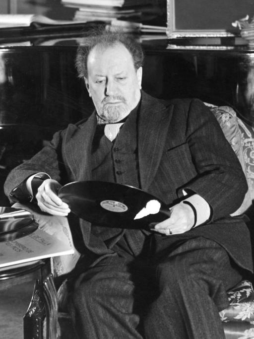 Sir Henry Joseph Wood sitzt in einem Sessel und hält eine Schallplatte in den Händen.