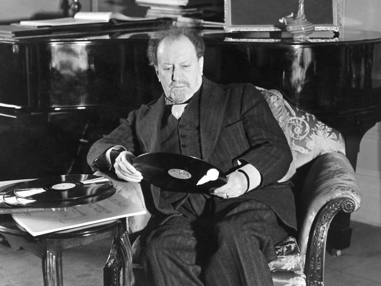 Sir Henry Joseph Wood sitzt in einem Sessel und hält eine Schallplatte in den Händen.