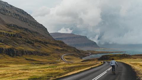 Ein junger Mann fährt mit seinem Skateboard eine Straße am Meer entlang. Ein junger Mann fährt mit seinem Skateboard eine Straße am Meer entlang.