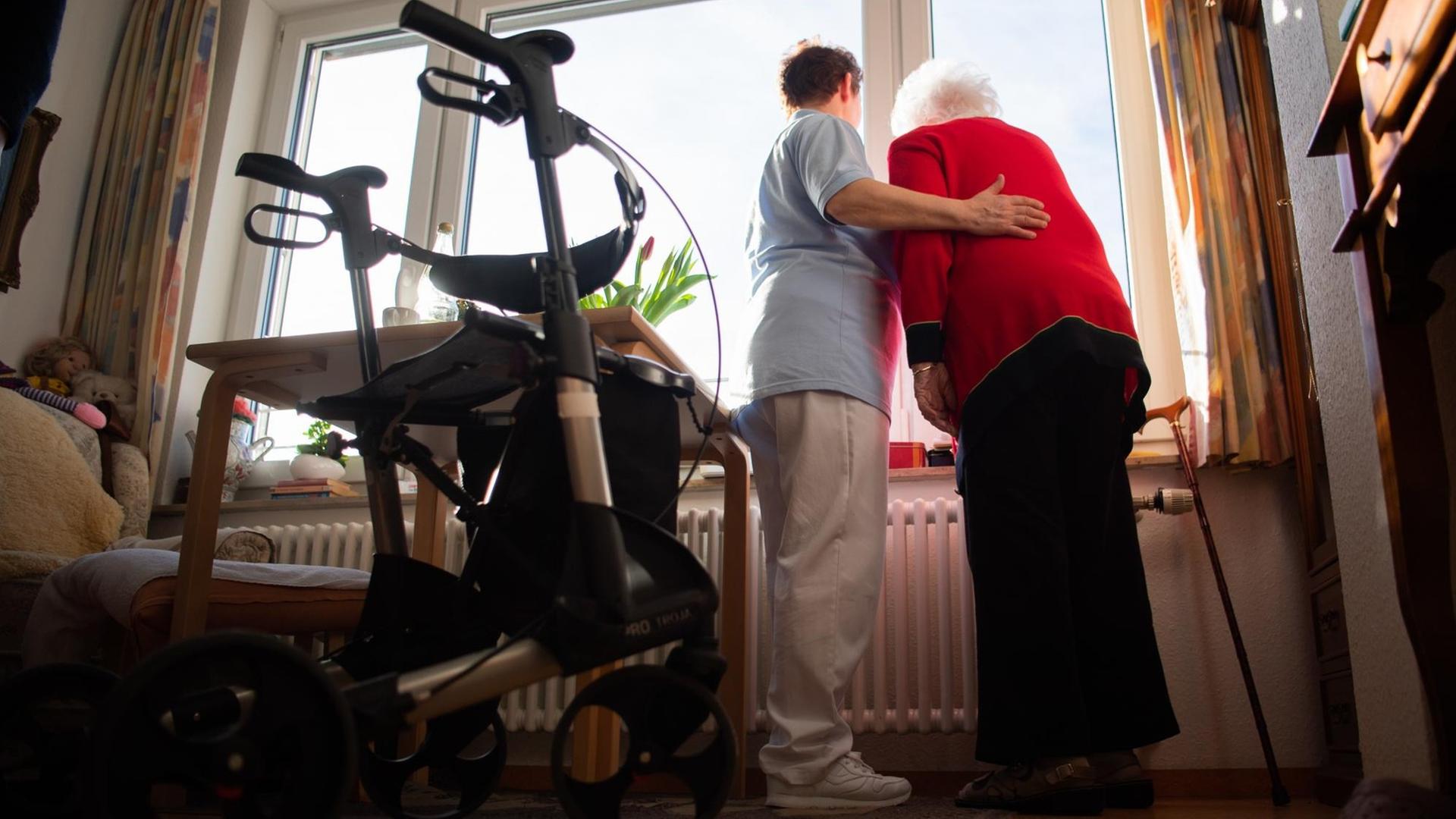 Baden-Württemberg, Böblingen: Eine Pflegerin (l.) und eine Bewohnerin des Pflegeheims schauen zusammen aus einem Fenster im Wohnbereich des Pflegeheims. Im Vordergrund steht ein Rollator