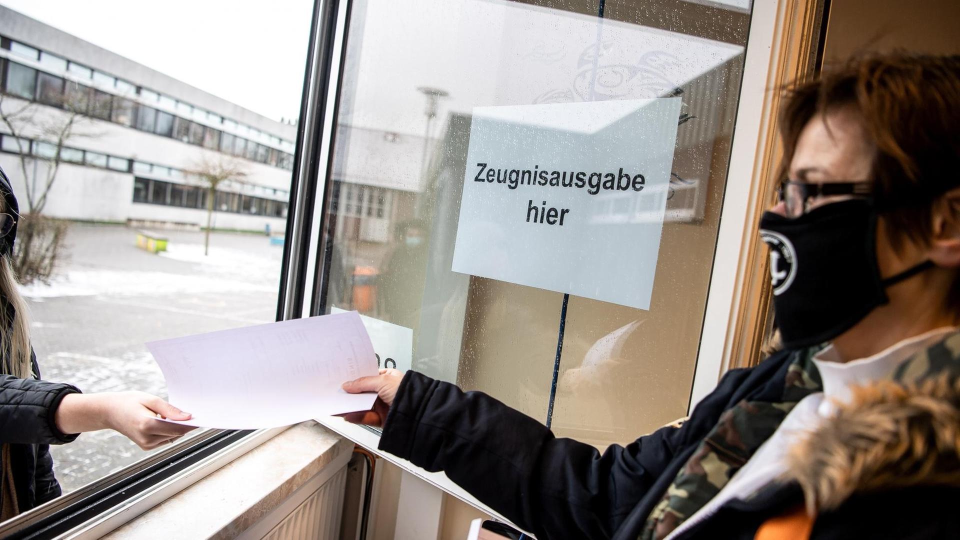 Kerstin Schermer, Sekretärin an der Oberschule Rodenkirchen, reicht den Schülerinnen und Schülern die Zeugnisse aus dem Sekretariats-Fenster.