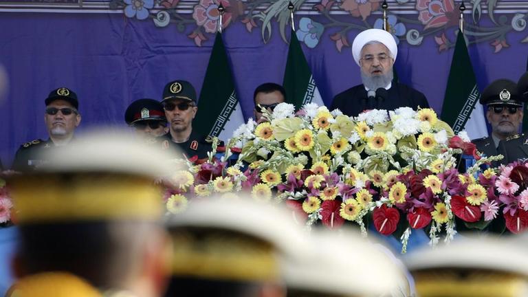 Soldaten stehen in Reih und Glied vor einer Bühne, auf der Rohani seine Ansprache hält. Das Foto ist auf den Präsidenten scharf gestellt.