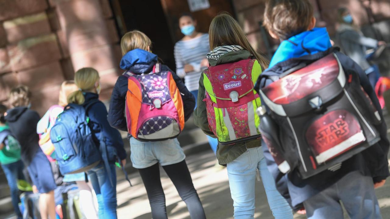 Frankfurt am Main: Schülerinnen und Schüler einer vierten Klasse der Linnéschule werden auf dem Schulhof von ihrer lassenlehrerin begrüßt, die einen Mundschutz trägt.