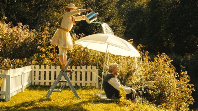 Szene aus dem Film "Nur ein Tag": Aljoscha Stadelmann sitzt unter einem Sonnenschirm an einem Ufer, Karoline Schuch schüttet mit einer Gieskanne Wasser über den Schirm