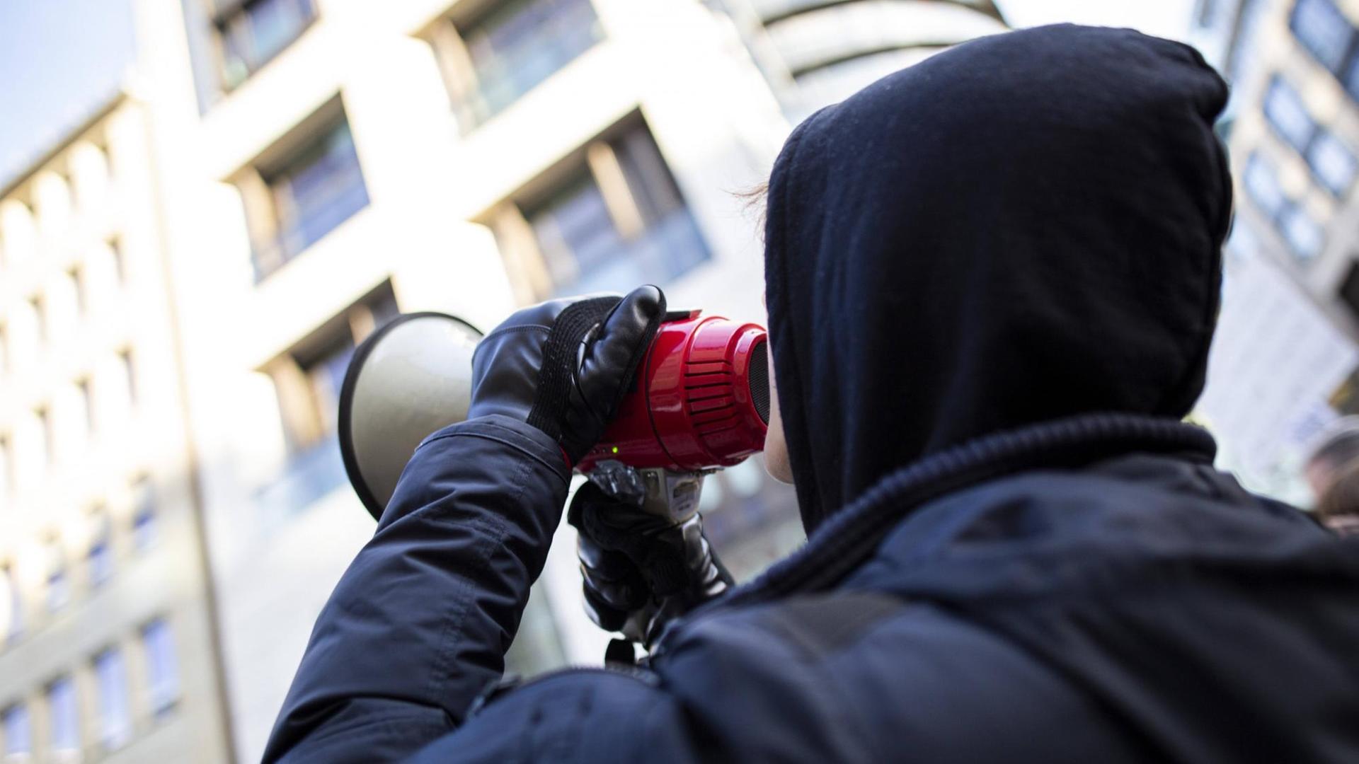 Ein junger Mann trägt Kapuzenpulli und ruft in ein Megaphon