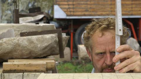 Auf dem Bild ist der Steinmetz Michael Spengler bei der Arbeit zu sehen. Aufmerksam misst er einen Stein mit einem Zollstock ab.