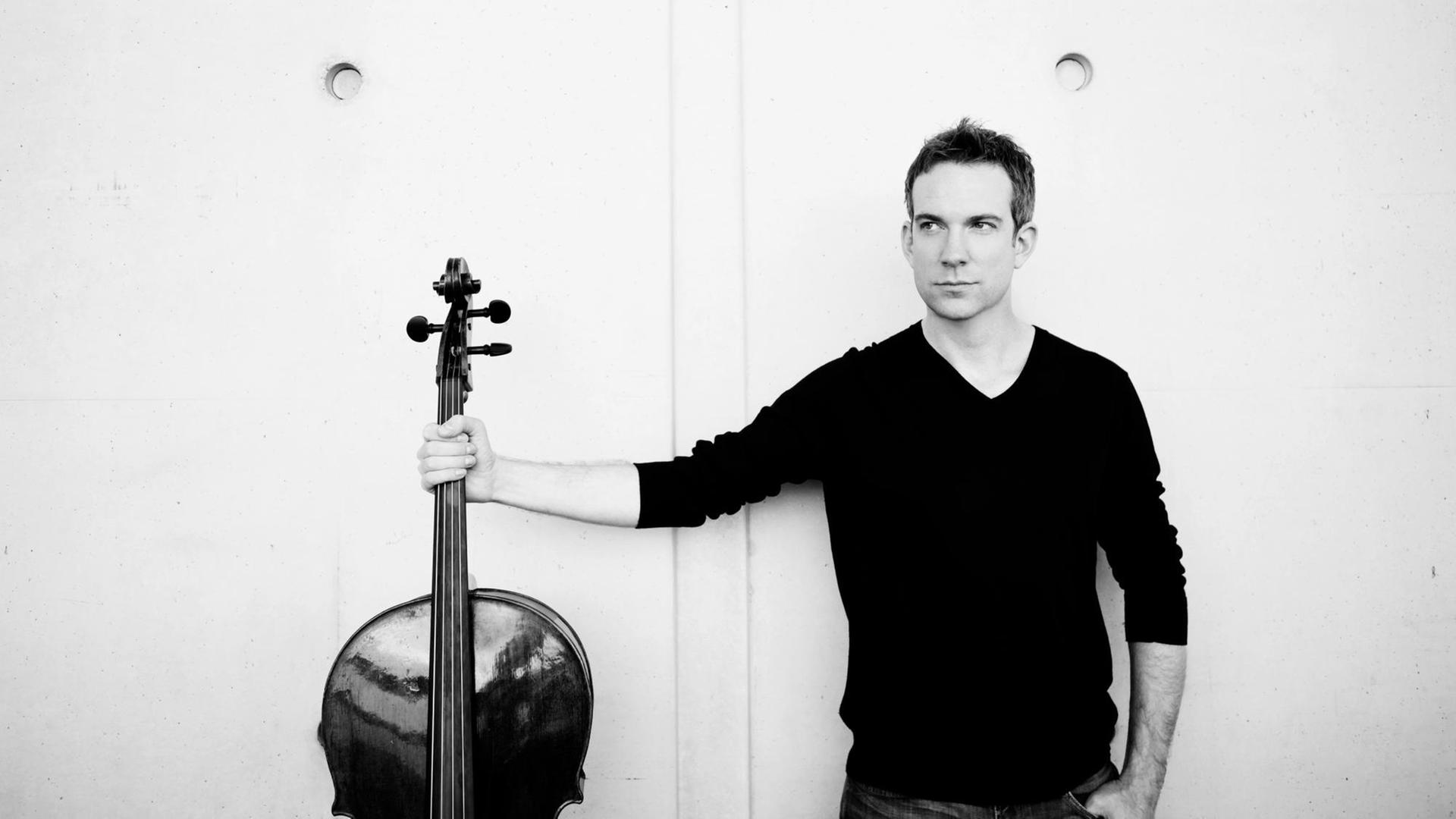 Schwarz-weiß Aufnahme von Johannes Moser, der in seiner rechten Hand ein Cello hält