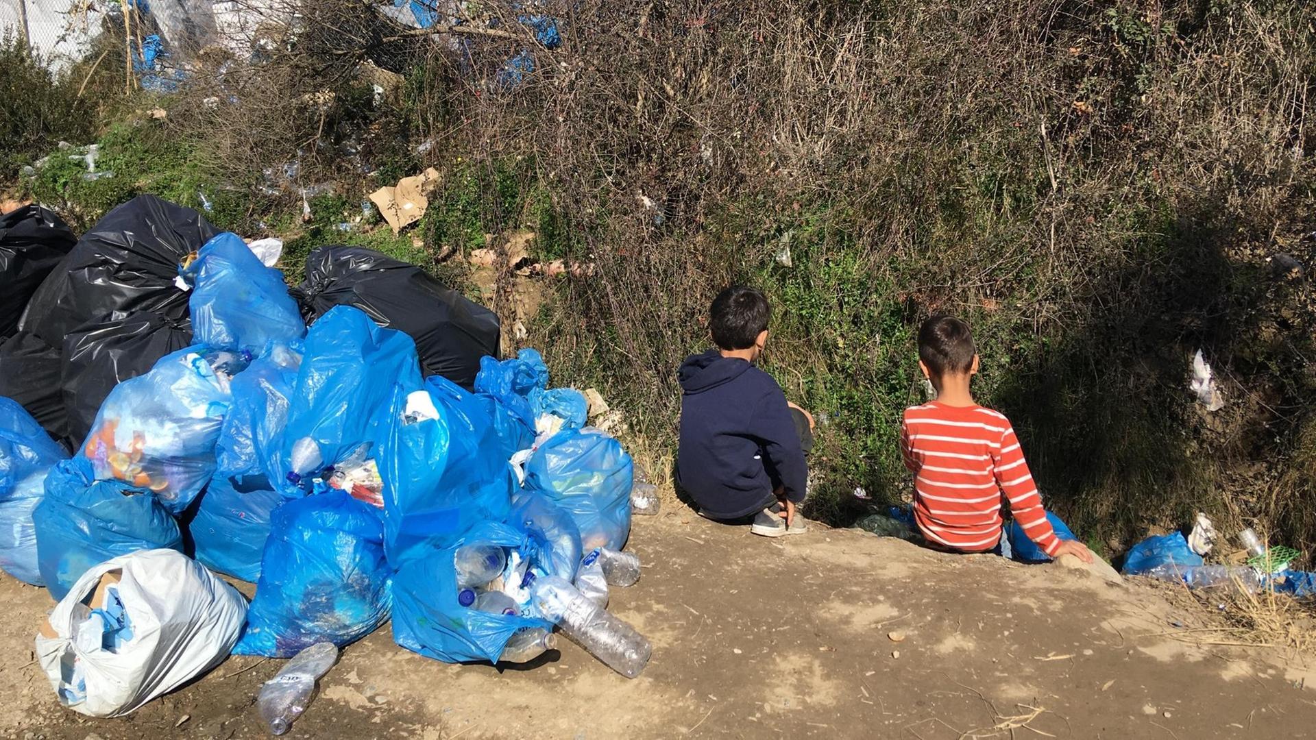 Kinder sitzen in einem Flüchtlings-Lager in Griechenland. Neben den Kinder liegt Müll.