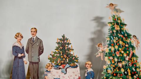 Ankleidepuppen mit Kleidungsstücken stehen an einem Spielzeugweihnachtsbaum mit Geschenken. 