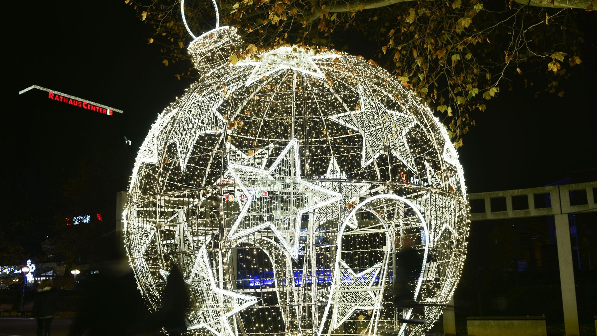 Besucher laufen am 24.11.2014 in Ludwigshafen (Rheinland-Pfalz) an einer begehbaren, beleuchteten Weihnachtskugel vorbei. Nach Angaben der Stadt handelt es sich um die größte ihrer Art in Deutschland. Sie besteht aus einem fünf Meter hohen, runden Metallgerippe, um das herum 20 000 LED-Lichter angebracht sind.