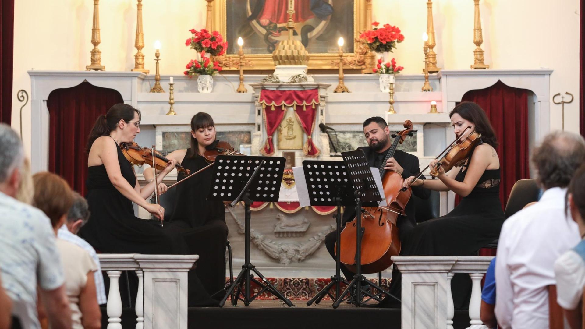 Drei Frauen mit Violinen und ein Mann mit Cello sitzen im Halbkreis um ihre Notenständer und spielen im Altarraum einer Kirche klassische Musik