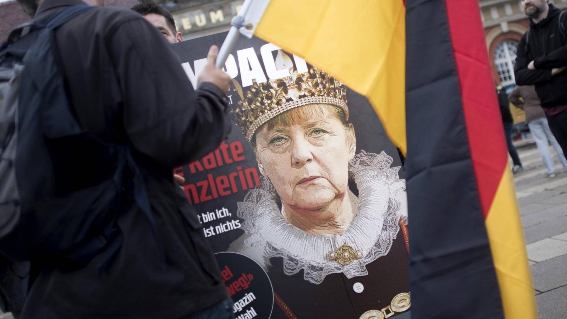 Auf einer Demonstration ist ein Anti-Merkel-Plakat zu sehen, im Vordergrund eine Deutschland-Flagge.
