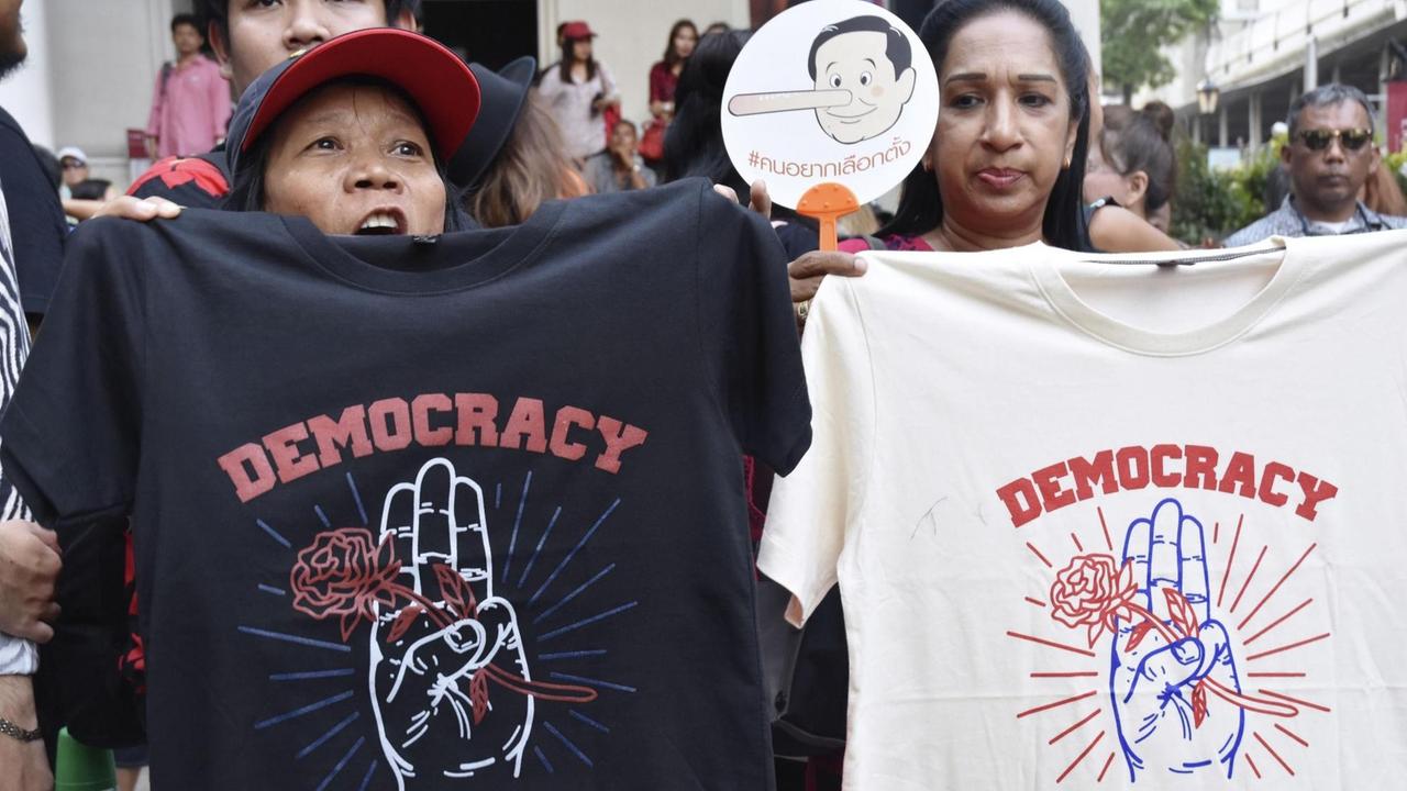 Zwei Demonstrantinnen halten T-Shirts mit der Aufschrift "Democracy" hoch. 