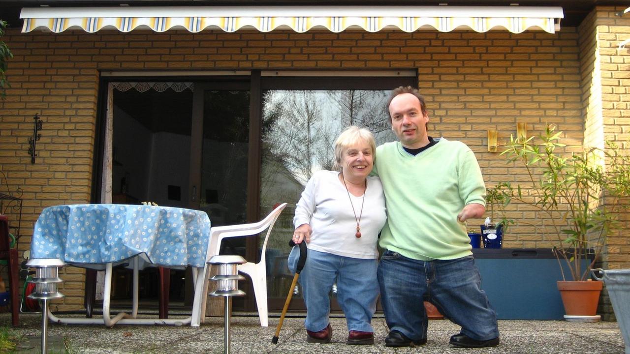 Eine Frau und ein Mann stehen auf einer Terrasse und halten sich im Arm.