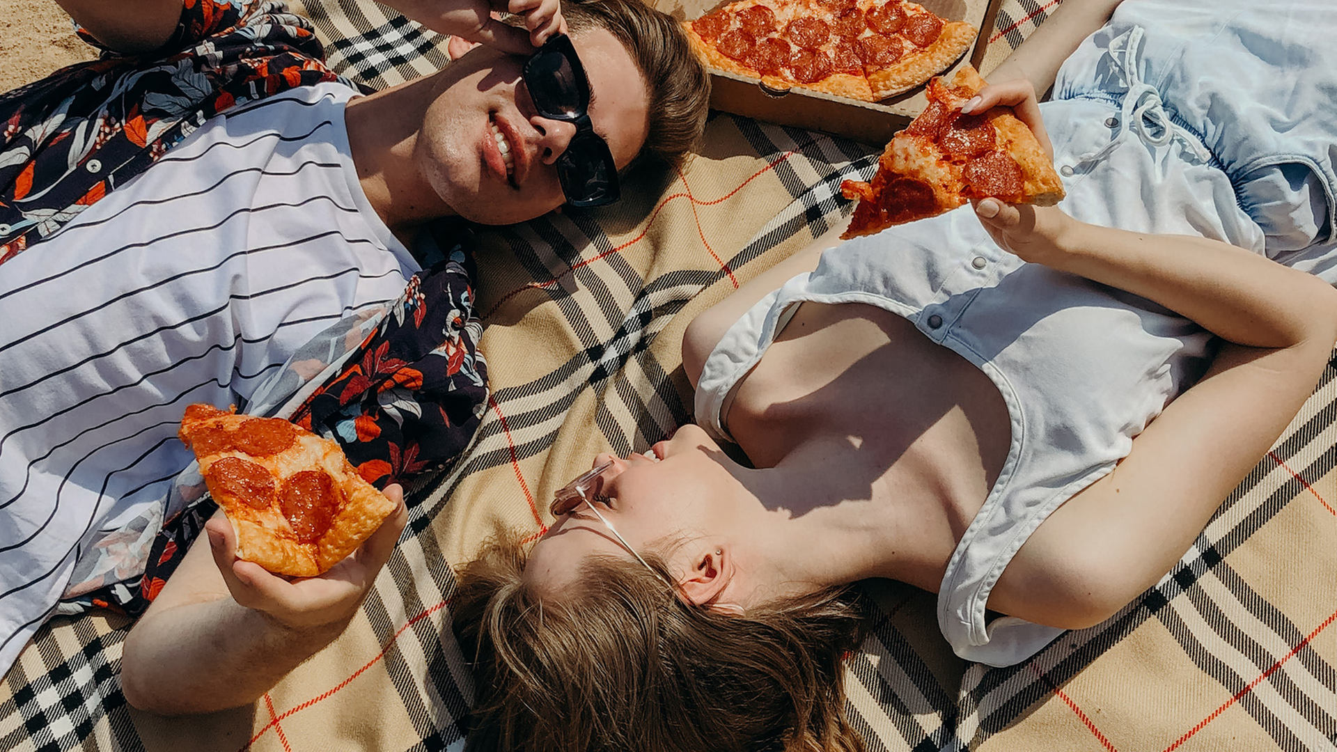 Ein junger Mann und eine junge Frau liegen mit einer Pizza auf der Decke.