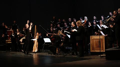 Das Ensemble La Tempête mit Solistinnen und Solisten, Chor und Orchester mit historischen Instrumenten, im Halbkreis aufgestellt.. Alle tragen schwarze Konzertkleidung. Der Dirigent hebt gerade die Hände zum Einsatz.