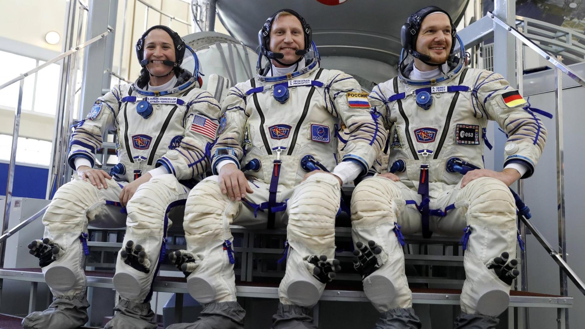 Die drei Astronauten sitzen in Astronautenanzügen vor einem Simulator im Yuri Gagarin-Trainingszentrum