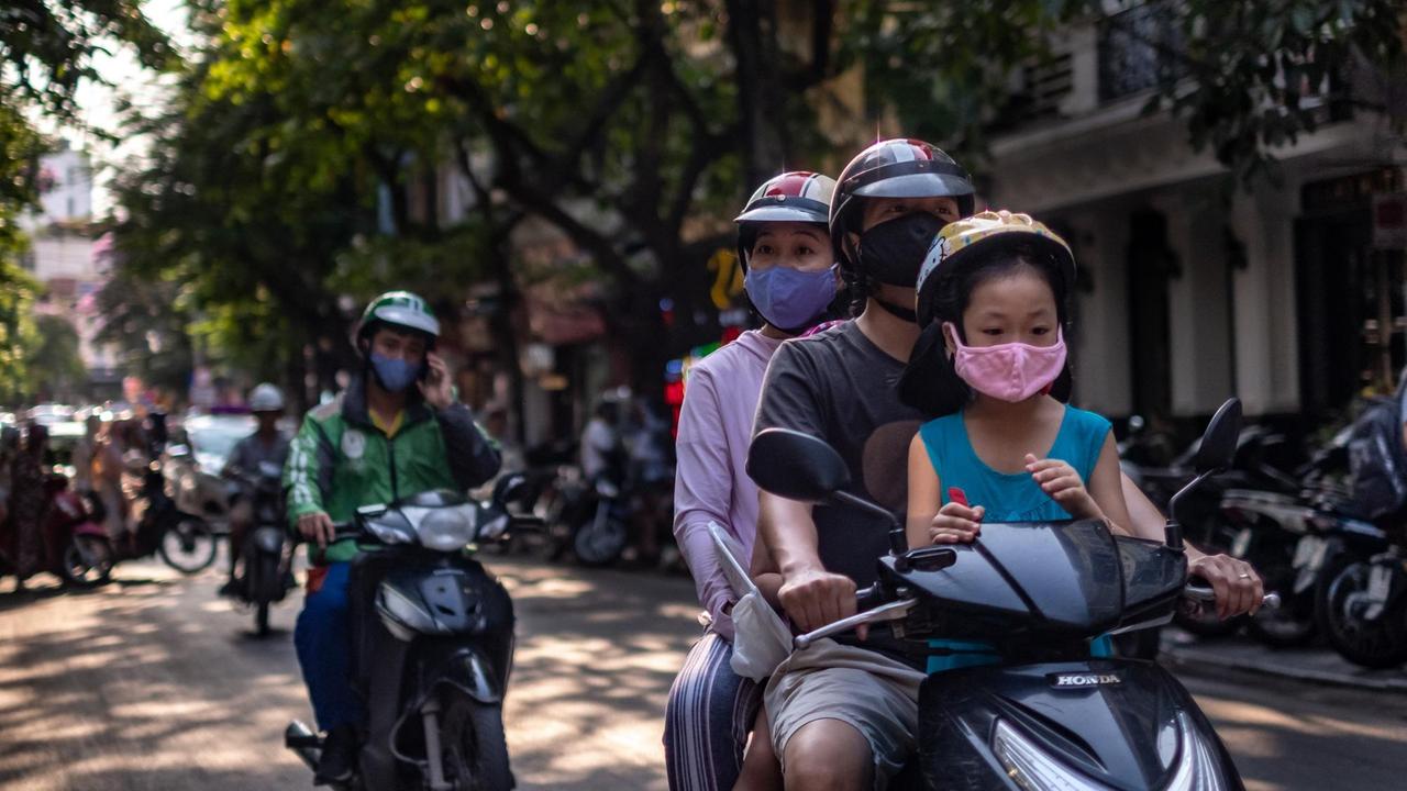 Eine Familie mit Gesichtsmasken auf einem Motorroller in der vietnameischen Hauptstadt Hanoi.