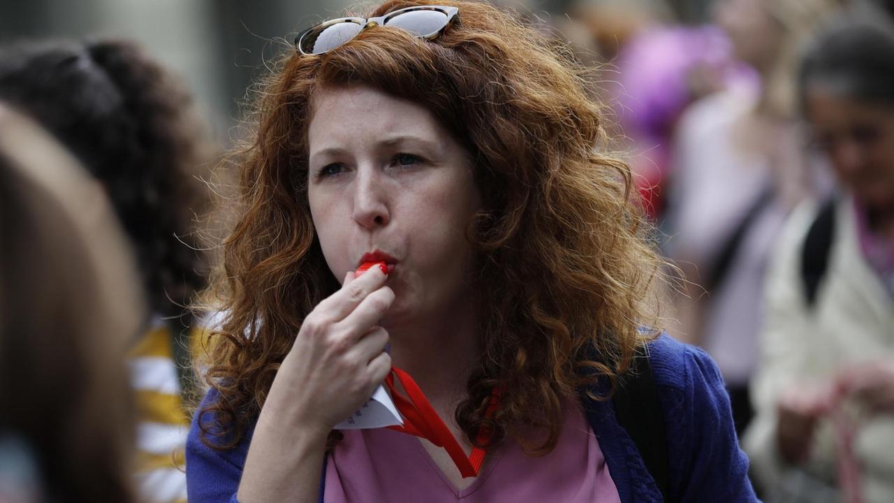 Eine rothaarige Frau bläst bei einer Demonstration in eine Trillerpfeife Eine rothaarige Frau bläst bei einer Demonstration in eine Trillerpfeife
